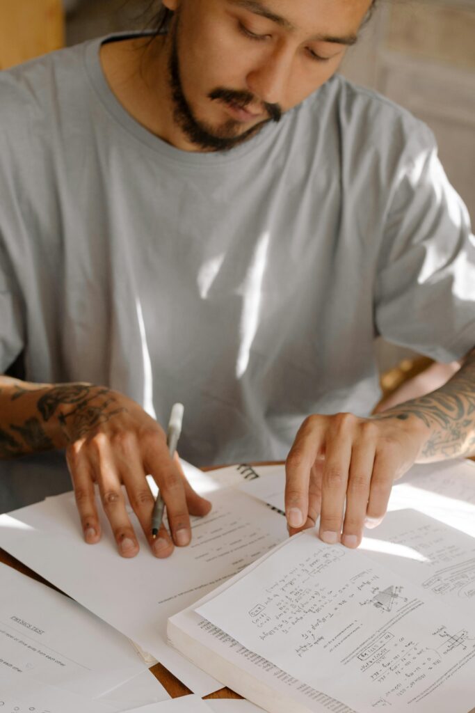 pexels-photo-4778624-4778624 Young adult with tattoos studying diligently with books and notes, highlighting concentration and learning.